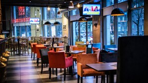 Un restaurante con piso a cuadros, varias mesas y sillas, y una pantalla de televisión mostrando un programa de noticias.