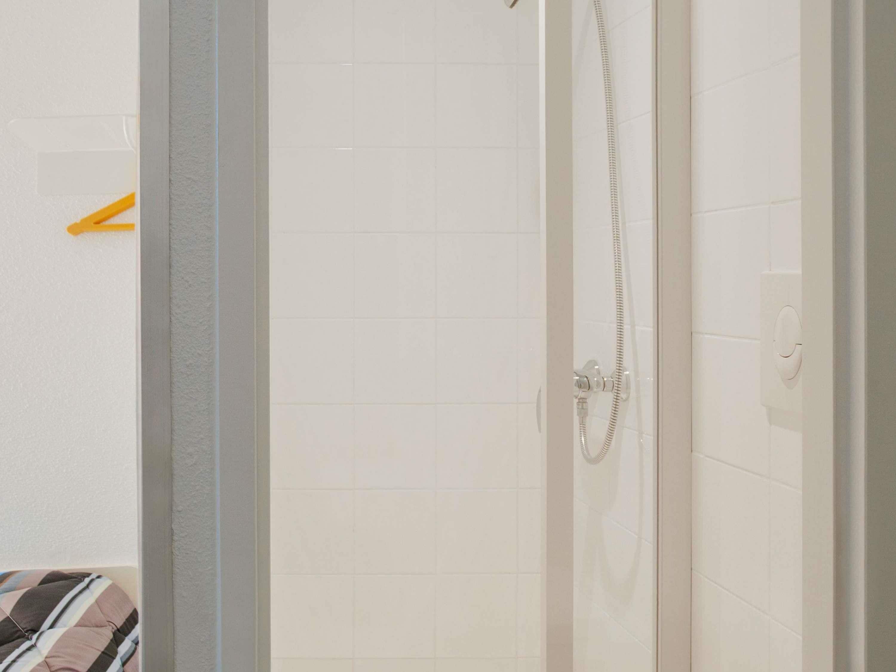 Un espacio de ducha con azulejos blancos, un cabezal de ducha y un panel de control.