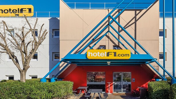 Un hotel con una entrada distintiva en azul y rojo, varias ventanas y un área de estar al aire libre visible.