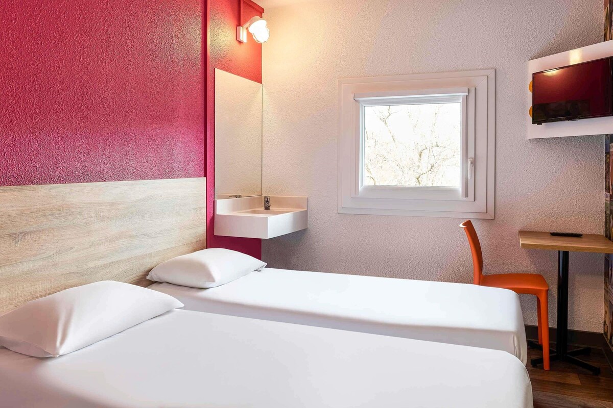 Una habitación de hotel con una cama, una ventana, un lavabo y una silla.