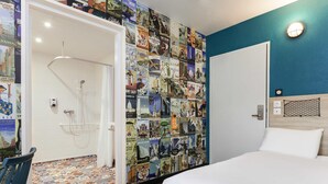 A hotel room with a bed, a shower, a wall decorated with travel posters, and a patterned floor. - hotelF1 Cholet (Cholet)