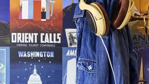 Una chaqueta vaquera con auriculares colgados en una pared decorada con carteles de viajes.