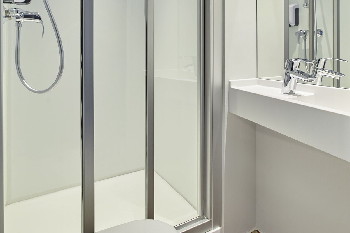 Un baño moderno con cabina de ducha de vidrio, un lavamanos blanco y un espejo grande.