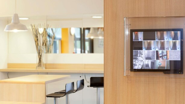 A modern interior with a wooden panel wall, a mounted security camera, and minimalist furniture. - hotelF1 Cholet (Cholet)