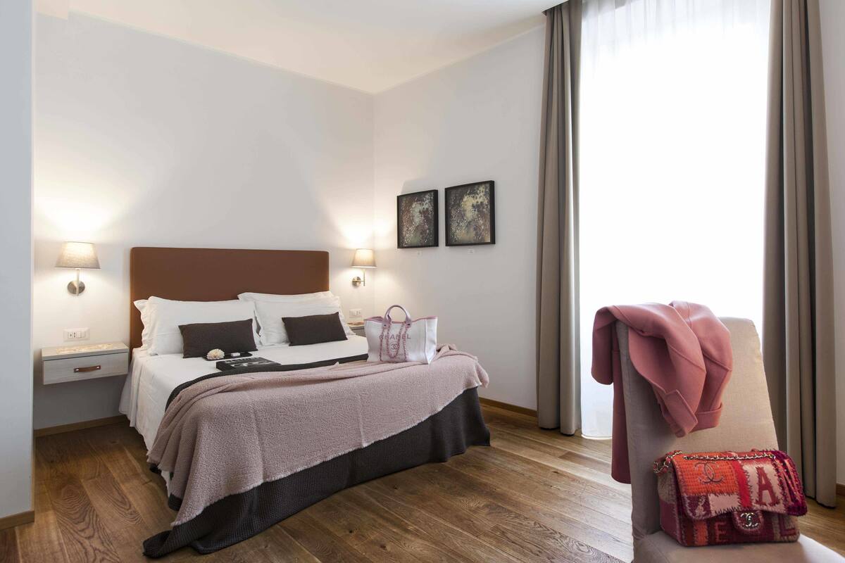 A neatly made bed with a brown headboard, a bedside lamp, and a decorative bag on the nightstand.