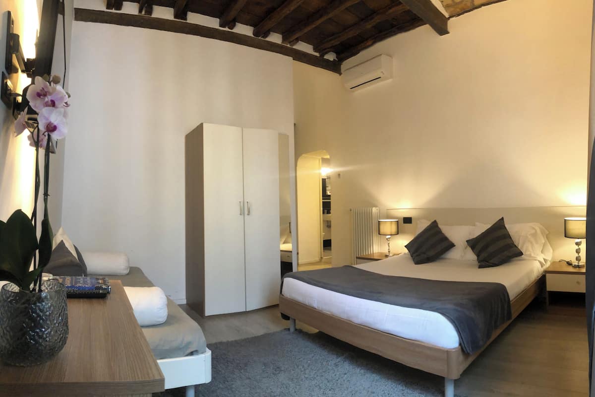A bedroom with a bed, bedside tables, a wardrobe, a desk with a vase, and a lamp.