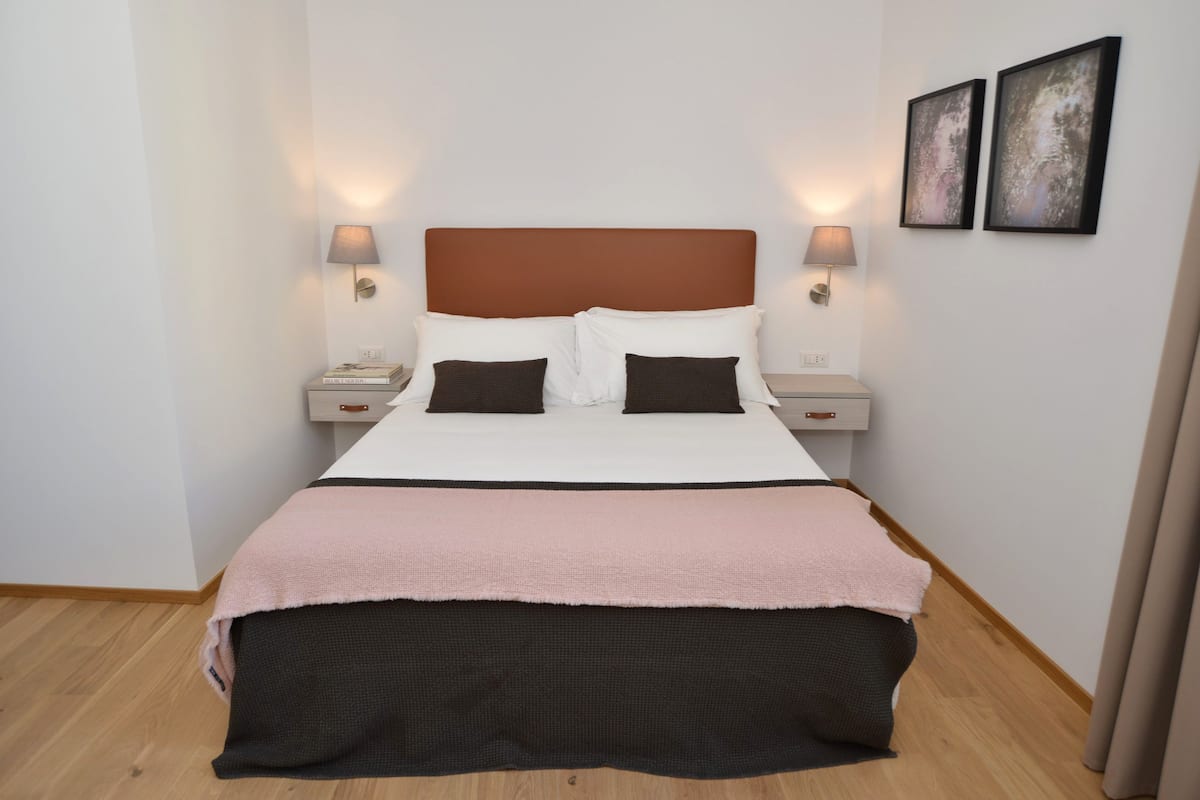 A neatly made bed with a pink and black bedspread, two bedside lamps, and two framed pictures on the wall.