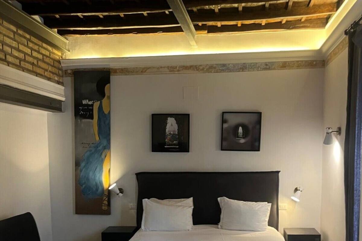 A bedroom with a large bed, two bedside tables, a nightstand, a black sofa, and a ceiling with exposed beams.