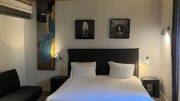 Un dormitorio con una cama grande, dos mesitas de noche, un aparador, un sofá negro y un techo con vigas a la vista.