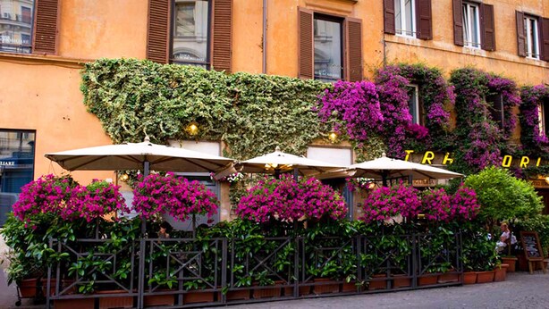 An outdoor cafe with tables and umbrellas, surrounded by lush greenery and vibrant flowers. - Giuturna Boutique Hotel (Rome)