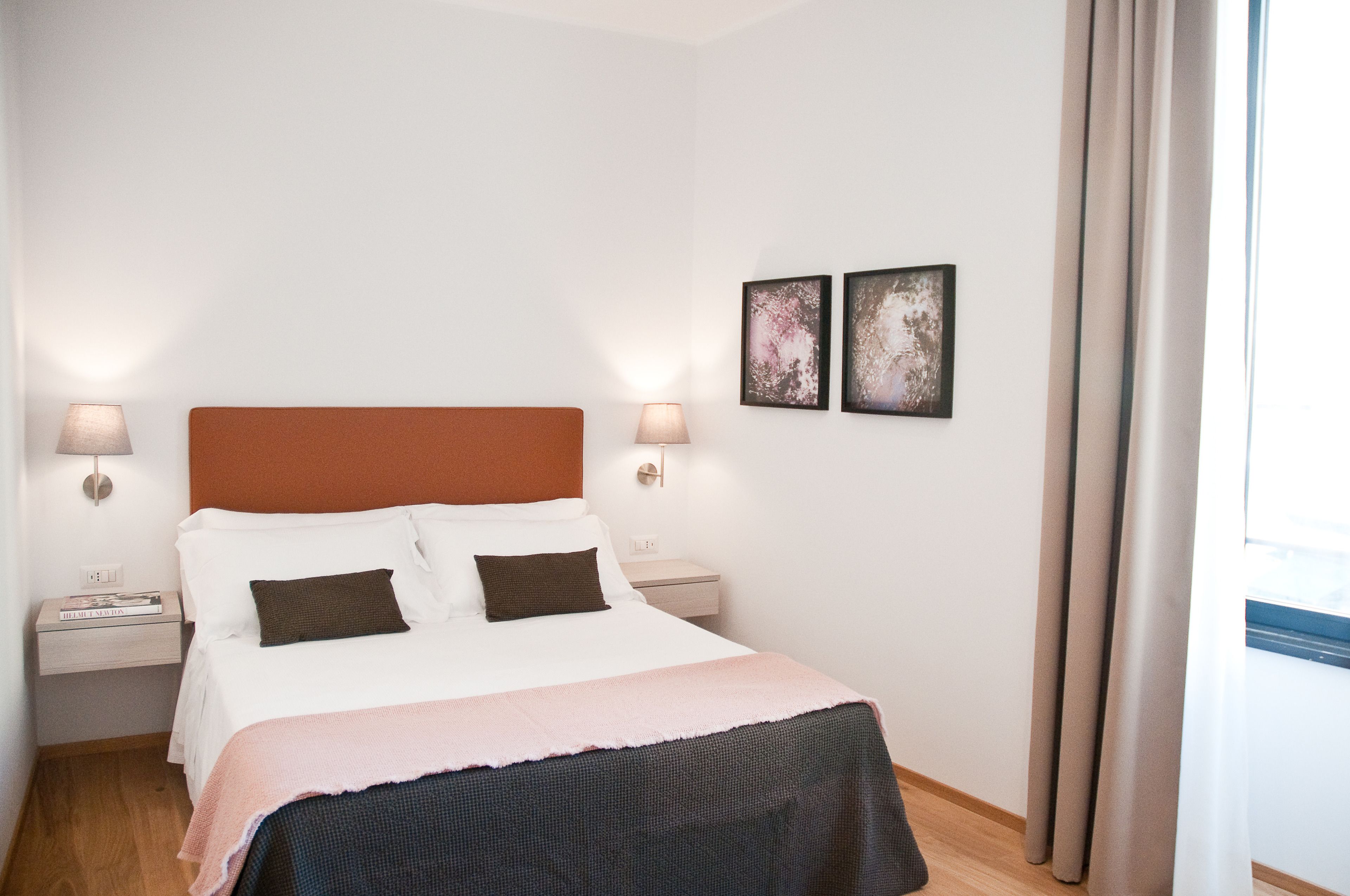A neatly made bed with a white and pink blanket, two bedside lamps, and two framed pictures on the wall.
