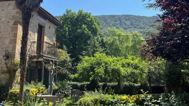 A stone building with a balcony, surrounded by lush greenery and a mountain in the background. - Posada Torre-Palacio de los Alvarado (Merindad de Montija)