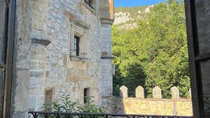 A stone building with arched windows and a balcony, surrounded by greenery and a stone wall. - Posada Torre-Palacio de los Alvarado (Merindad de Montija)
