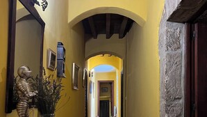 A hallway with wooden flooring, yellow walls, and a stone accent wall. There is a statue on a table, a mirror, and framed pictures on the walls. - Posada Torre-Palacio de los Alvarado (Merindad de Montija)
