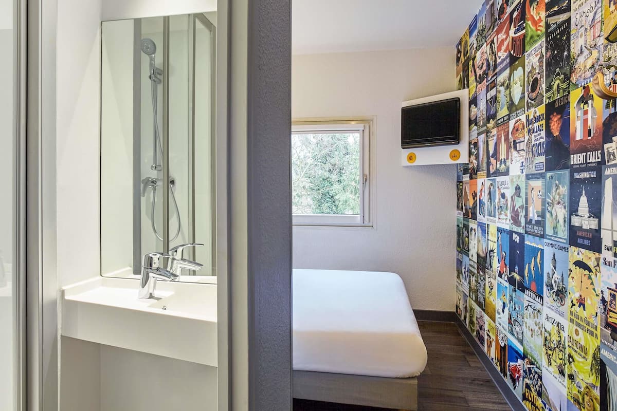 A bathroom with a shower, a sink, a toilet, a window, and a wall decorated with travel posters.