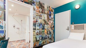 Une chambre d’hôtel avec un lit, une douche, un mur décoré d’affiches de voyage et un mur d’accent bleu.