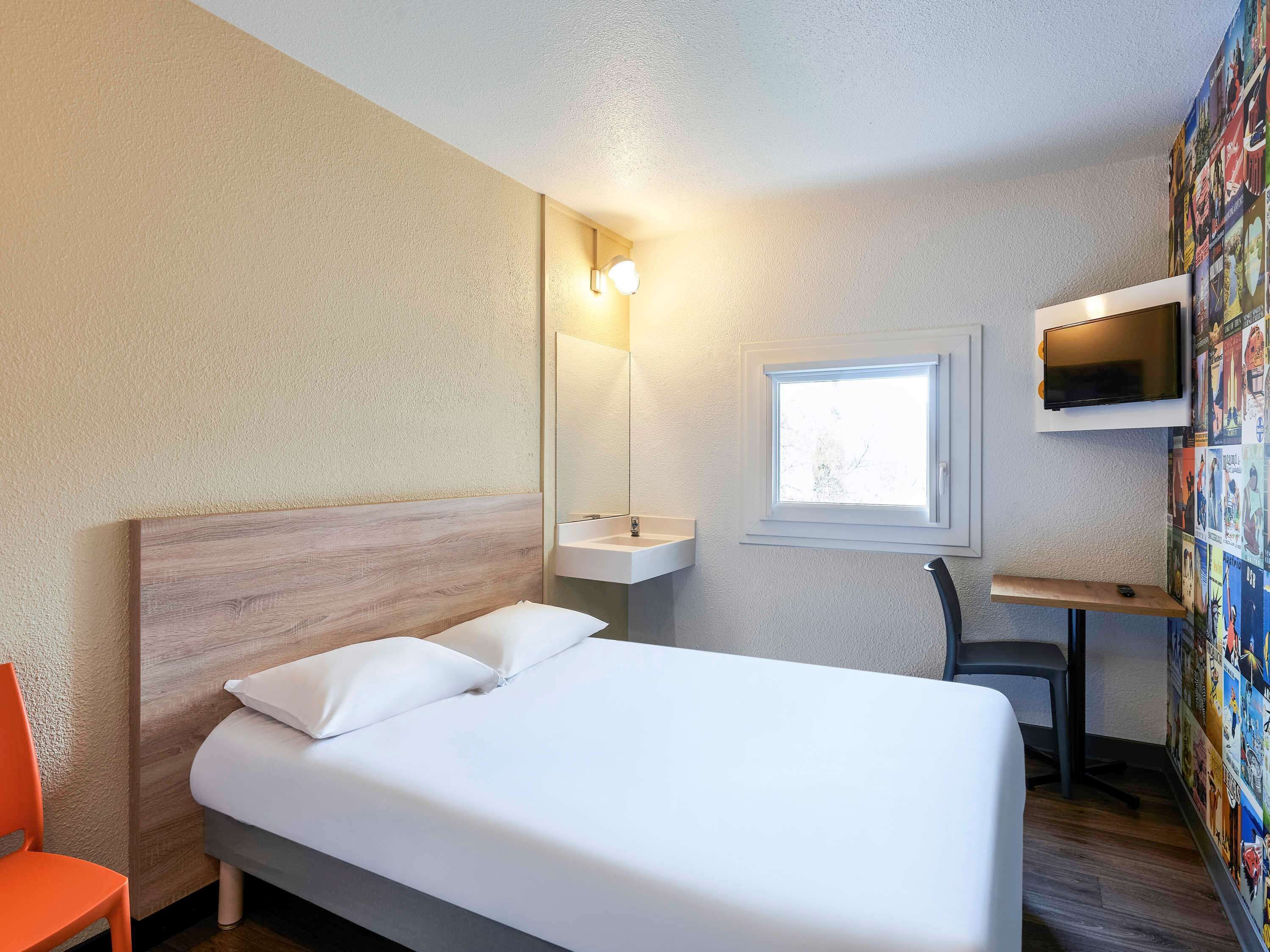 Ein Hotelzimmer mit Bett, Schreibtisch, Stuhl, Fernseher und Fenster.