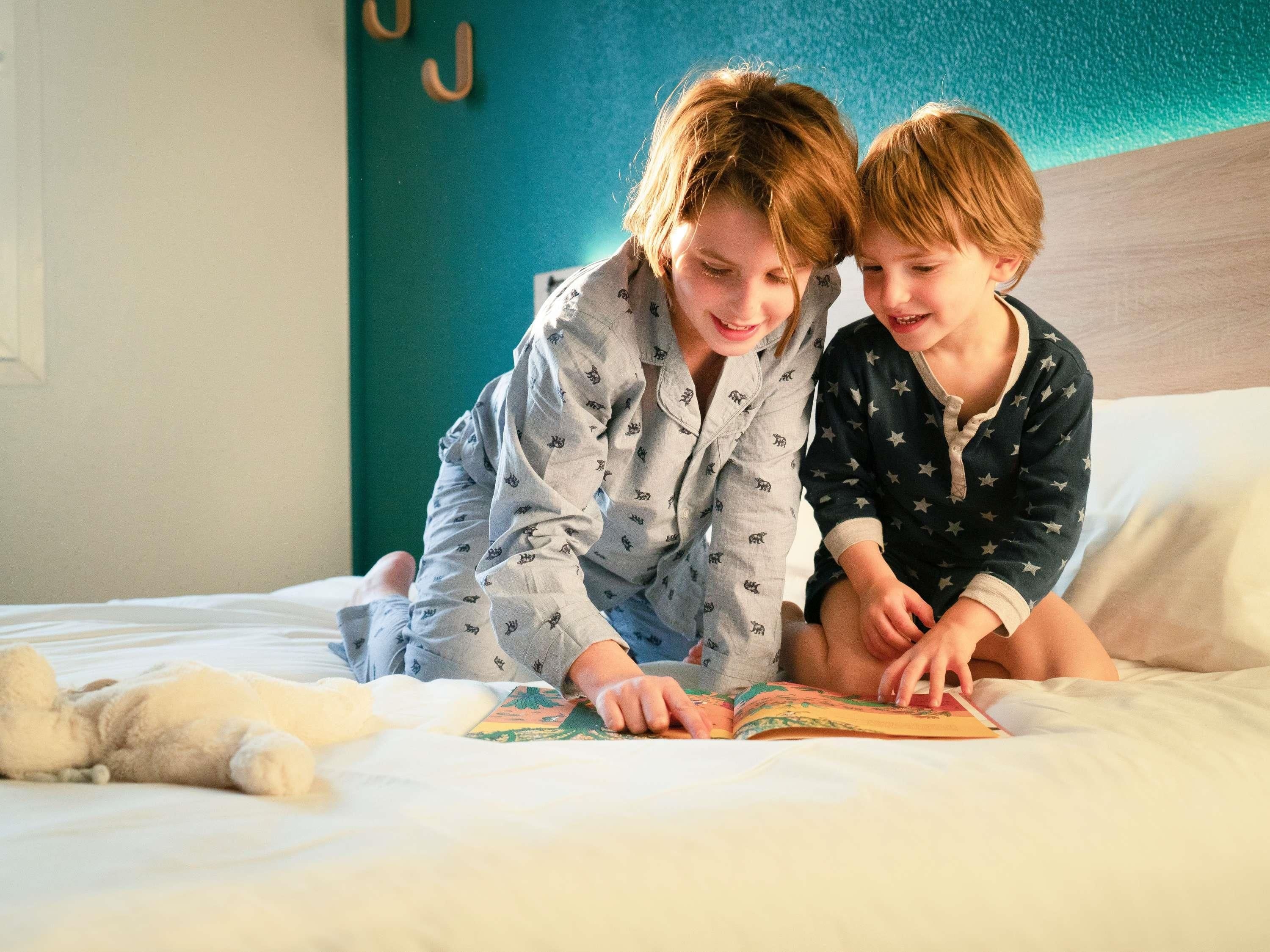 Dos personas leyendo un libro en una cama con un osito de peluche.