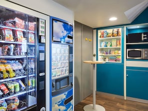 A vending machine with various food and drink options, a microwave, and a small shelf with snacks. - hotelF1 Villepinte Parc des Expositions (Villepinte)