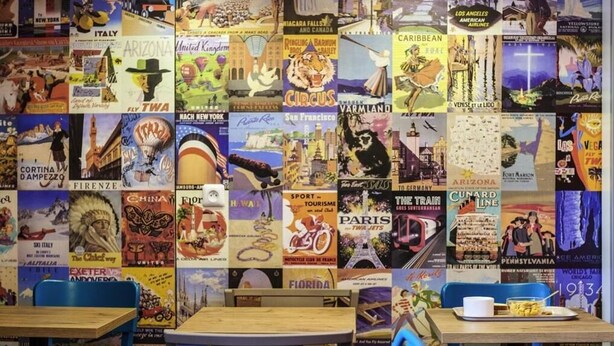 En væg dekoreret med gamle rejseplakater og kort, der viser destinationer som Italien, Arizona og Paris.