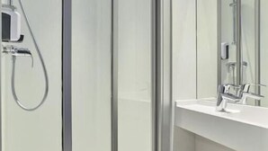 Et moderne badeværelse med en glasbrusekabine, et hvidt håndvask og flisegulv.