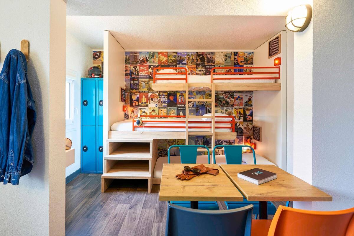 A bunk bed with posters, a desk with a book and sunglasses, and a chair.