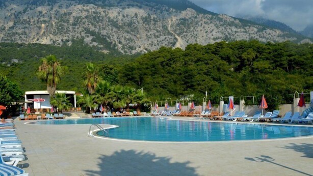 A swimming pool with lounge chairs and umbrellas, surrounded by greenery and mountains. - Magic Sun Hotel (Kemer)