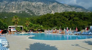 A swimming pool with lounge chairs and umbrellas, surrounded by greenery and mountains. - Magic Sun Hotel (Kemer)