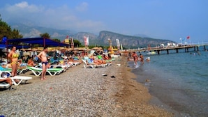 A beach with sun loungers and umbrellas, a pier extending into the water, and mountains in the background. - Magic Sun Hotel (Kemer)