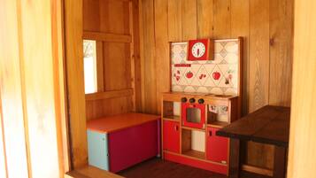Una habitación de madera con un armario rojo y azul, una pequeña zona de cocina con un reloj y una ventana.