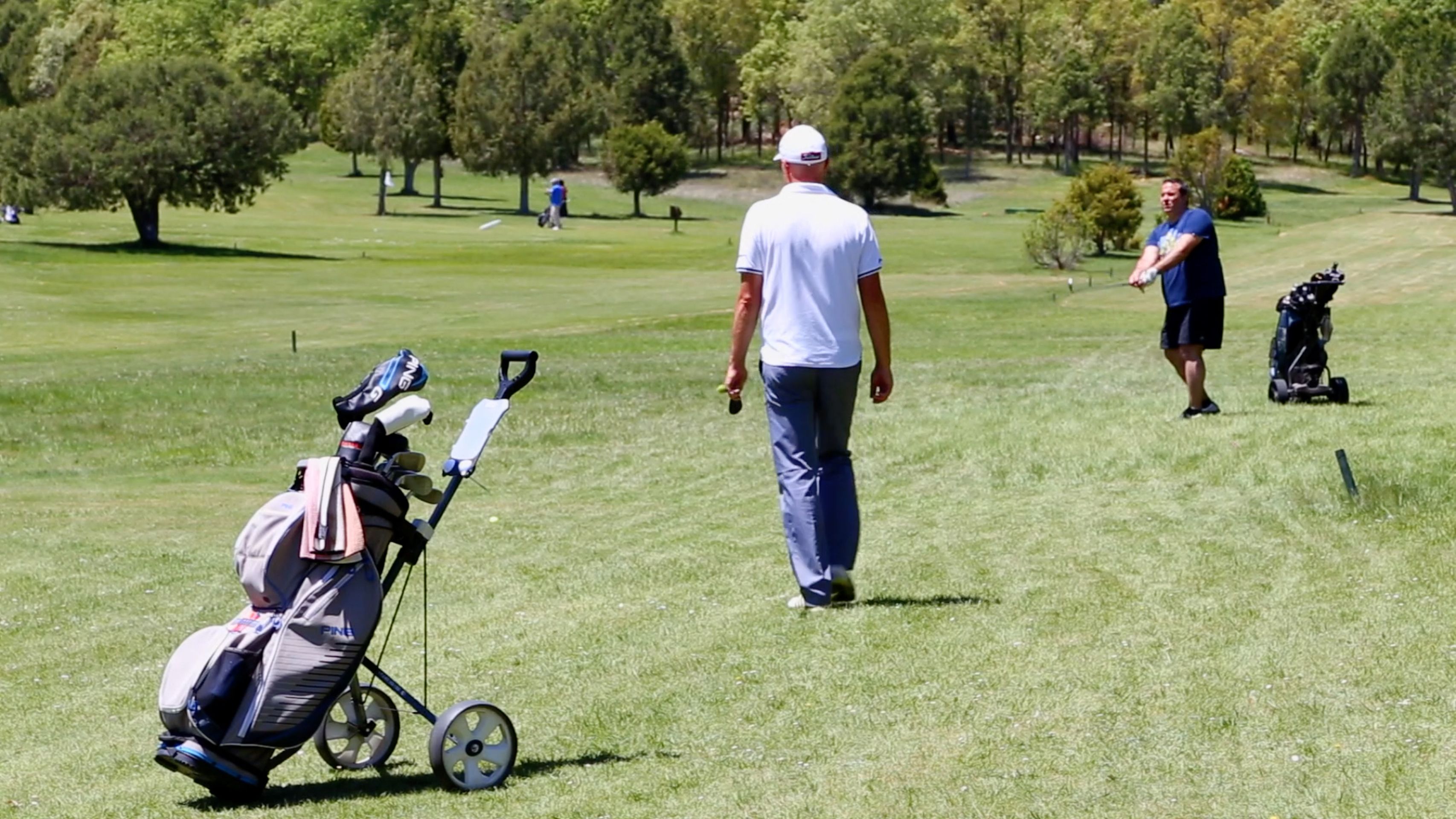 Un campo de golf con un cochecito de bebé, árboles y personas caminando.