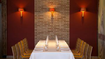 Un comedor con pared de ladrillo, dos lámparas de pared, una mesa larga con sillas y un mantel blanco.