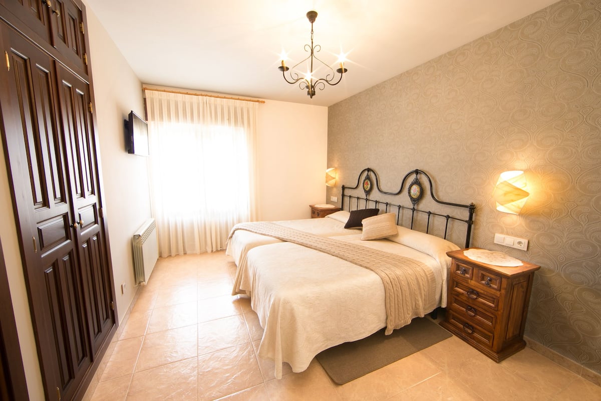 A bedroom with two beds, a dresser, a chandelier, and a window with curtains.
