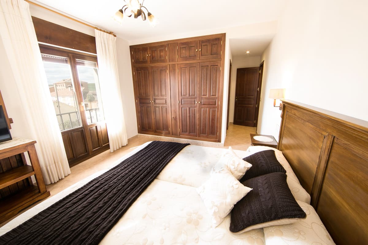 A bedroom with a large bed, wooden wardrobe, and a view through a window.
