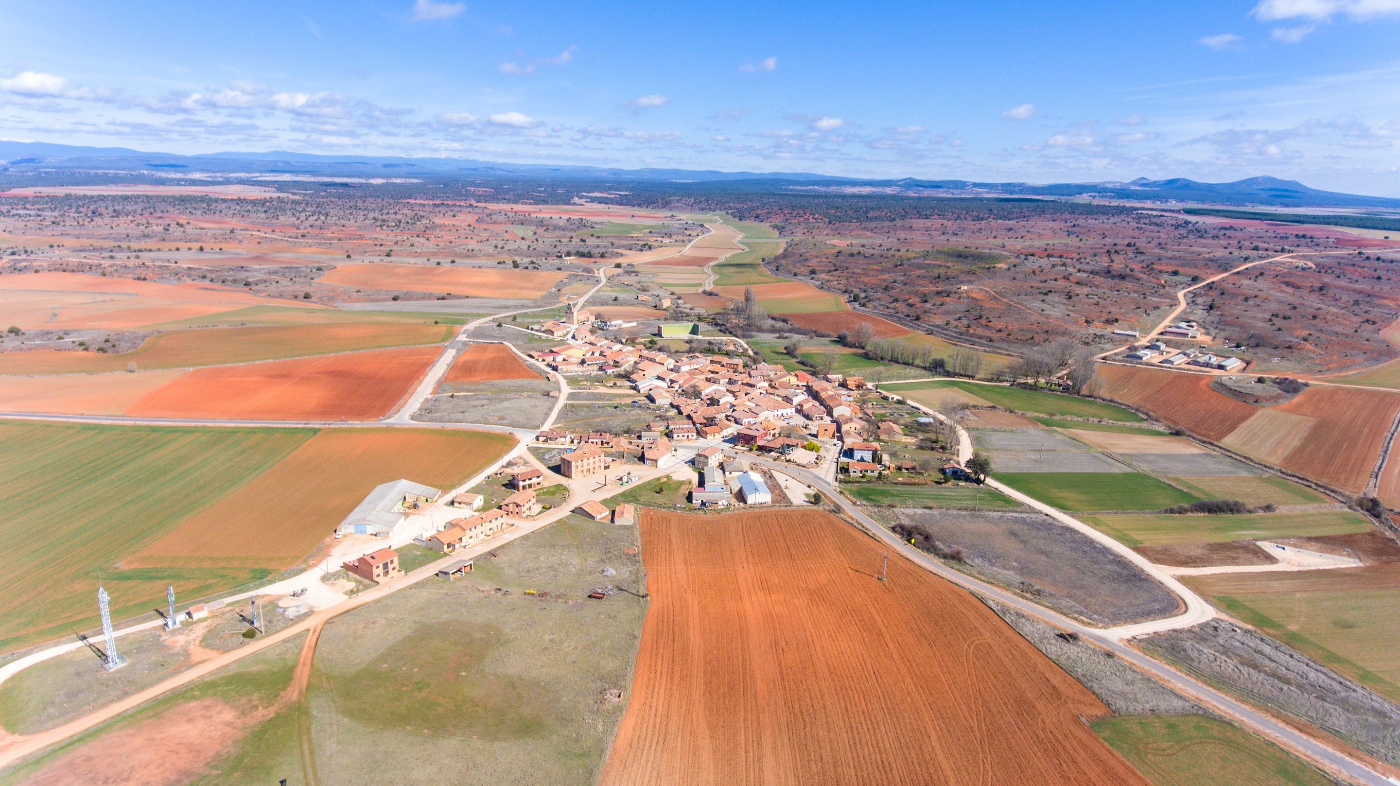 Vista aérea de un pueblo rural con un conjunto central de edificios rodeado de campos de cultivo.