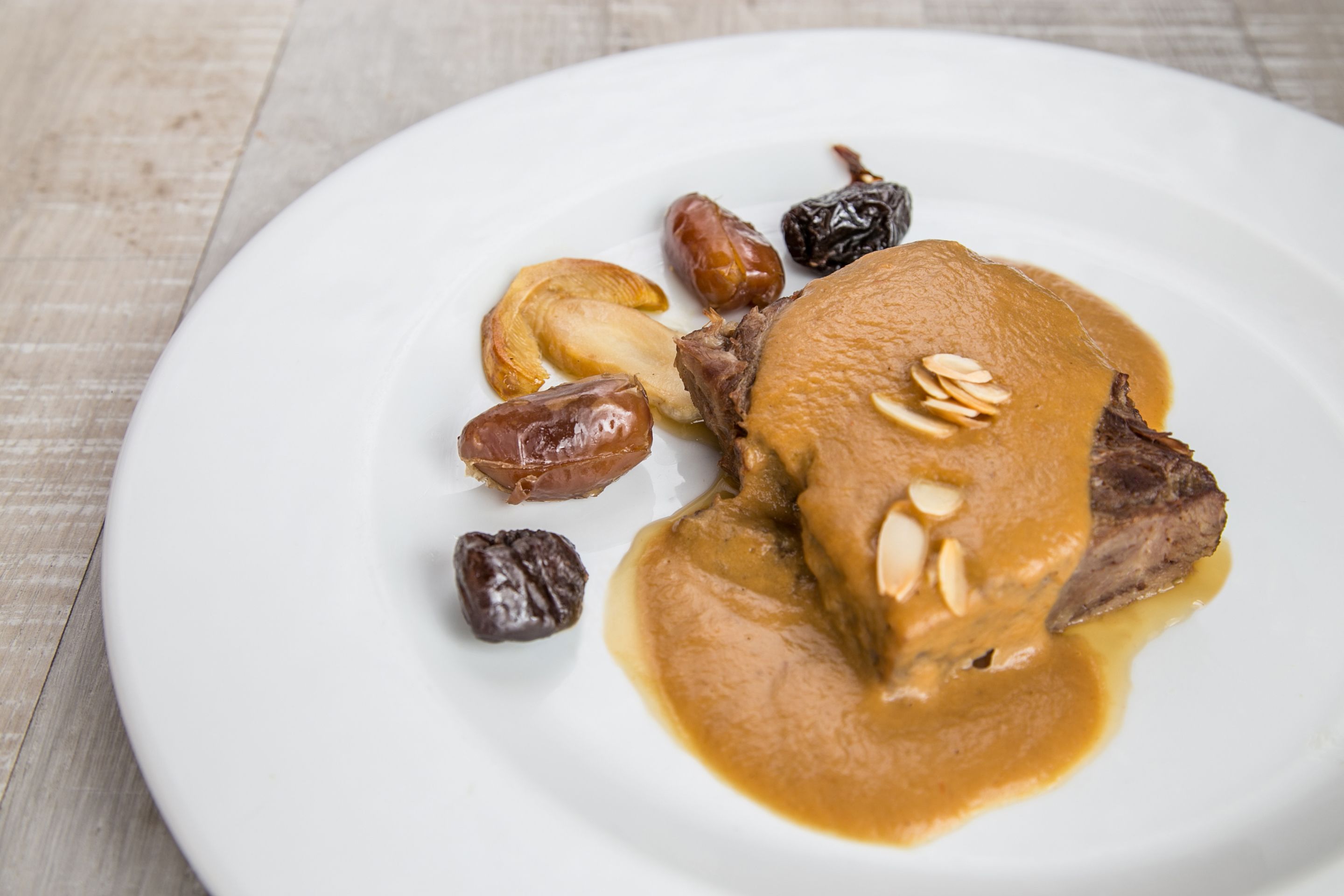 A plate with a piece of meat, a sauce, and dates.