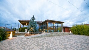 A modern house with a large glass facade, a stone pathway, and a small wooden structure in the foreground.