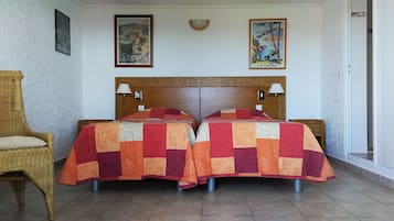 Een kamer met twee bedden, een rieten stoel en twee wandlampen.