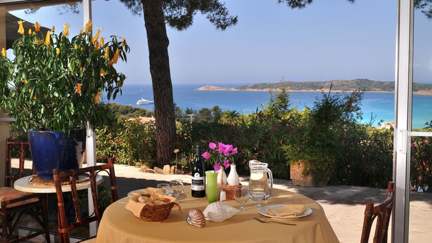 An outdoor dining area with a table set for two, featuring a view of the sea and hills. - Domaine Saint Pierre (Cargese)