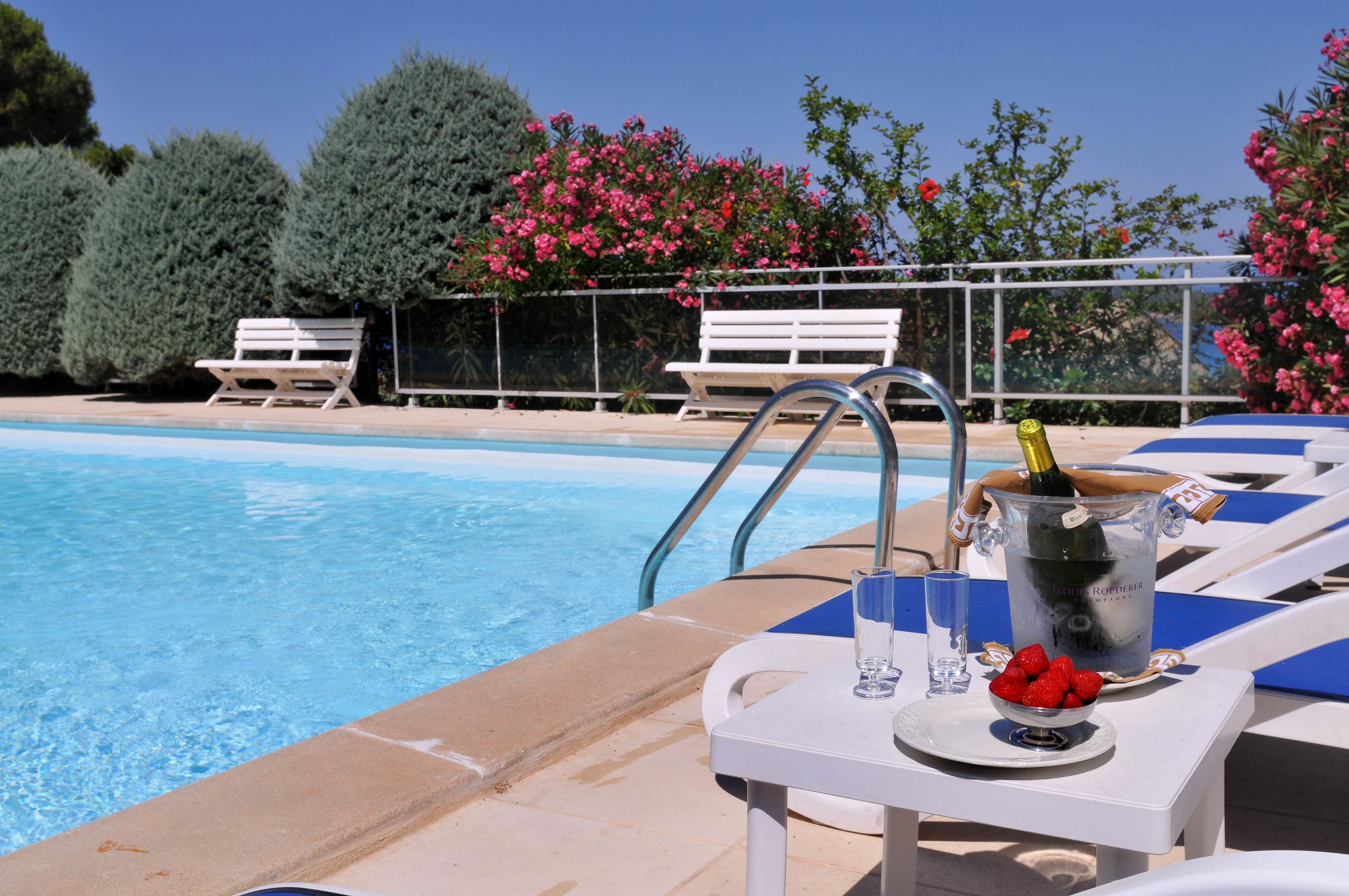 A poolside area with lounge chairs, a table with a bottle of champagne, strawberries, and a glass of water.