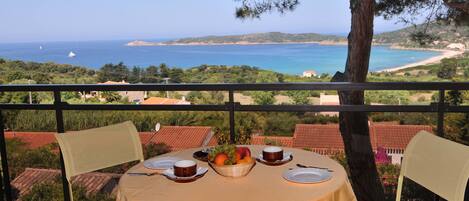 Une table dressée pour deux personnes, avec vue sur la mer et les collines.