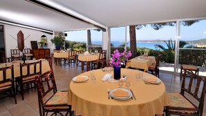 A dining area with round tables set for four, each with a tablecloth, chairs, and table settings. - Domaine Saint Pierre (Cargese)