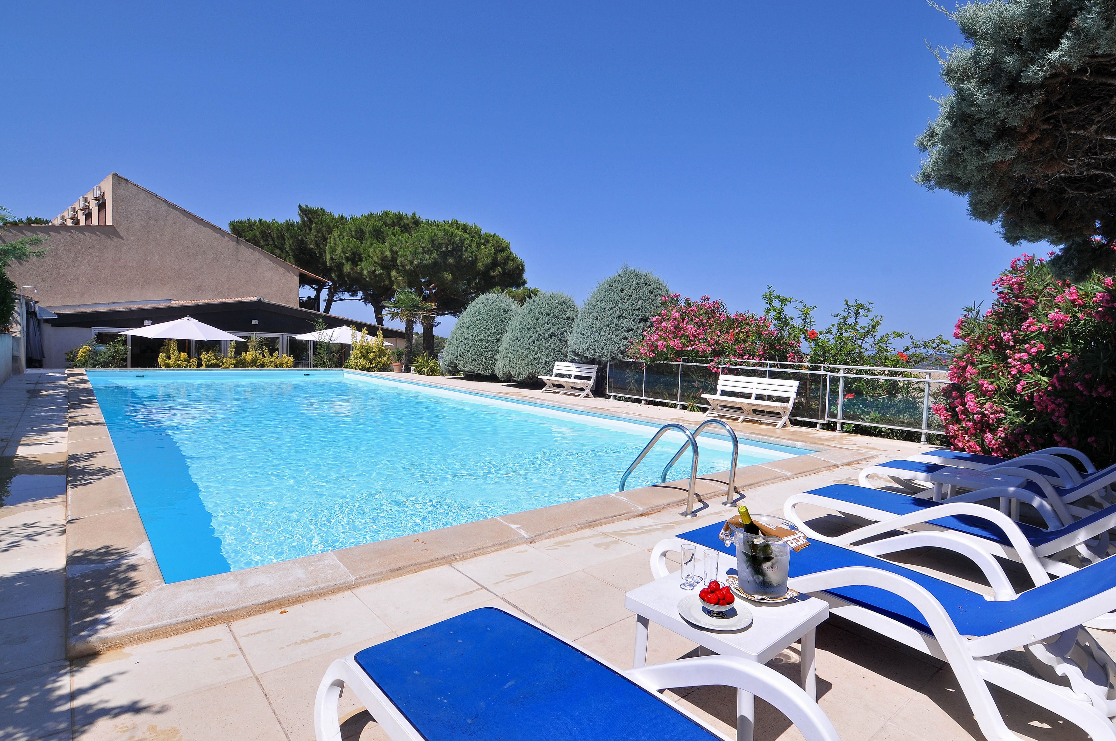 A swimming pool with lounge chairs and a table, surrounded by trees and a building.