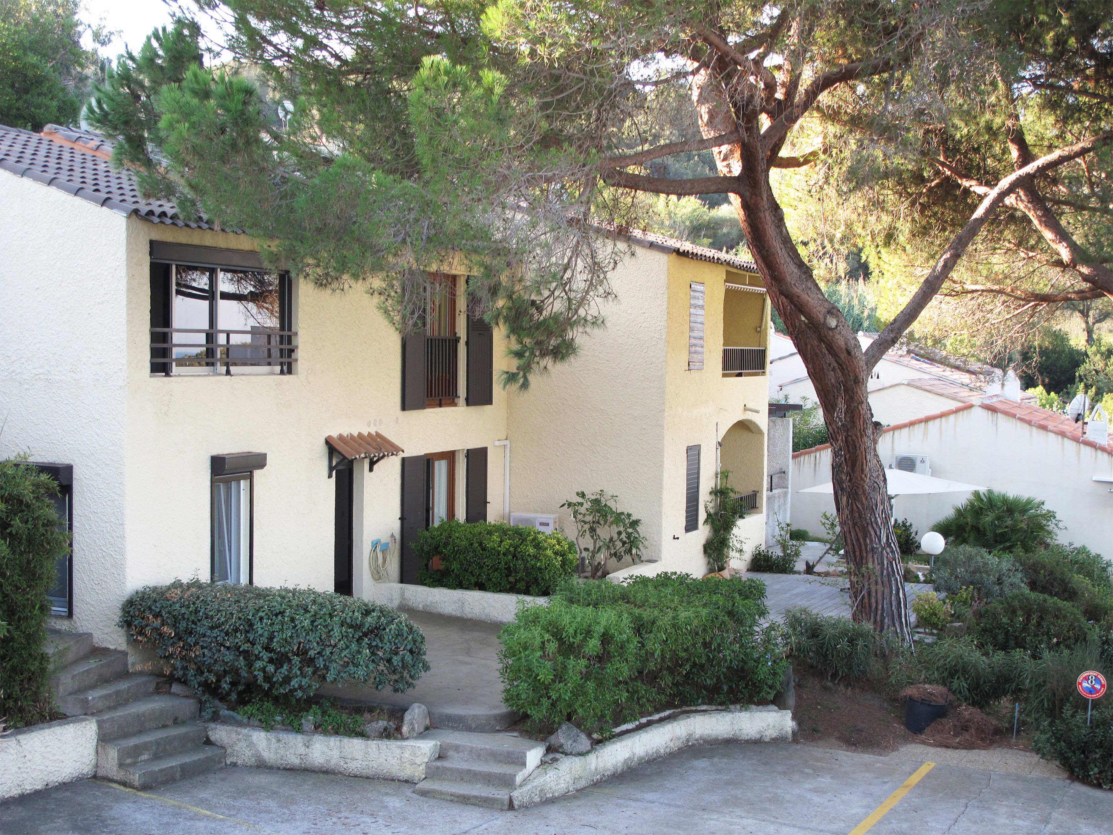 A two-story building with a yellow facade, multiple windows with shutters, and a tree in the foreground.