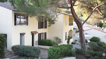 A two-story building with a yellow facade, multiple windows with shutters, and a tree in the foreground.