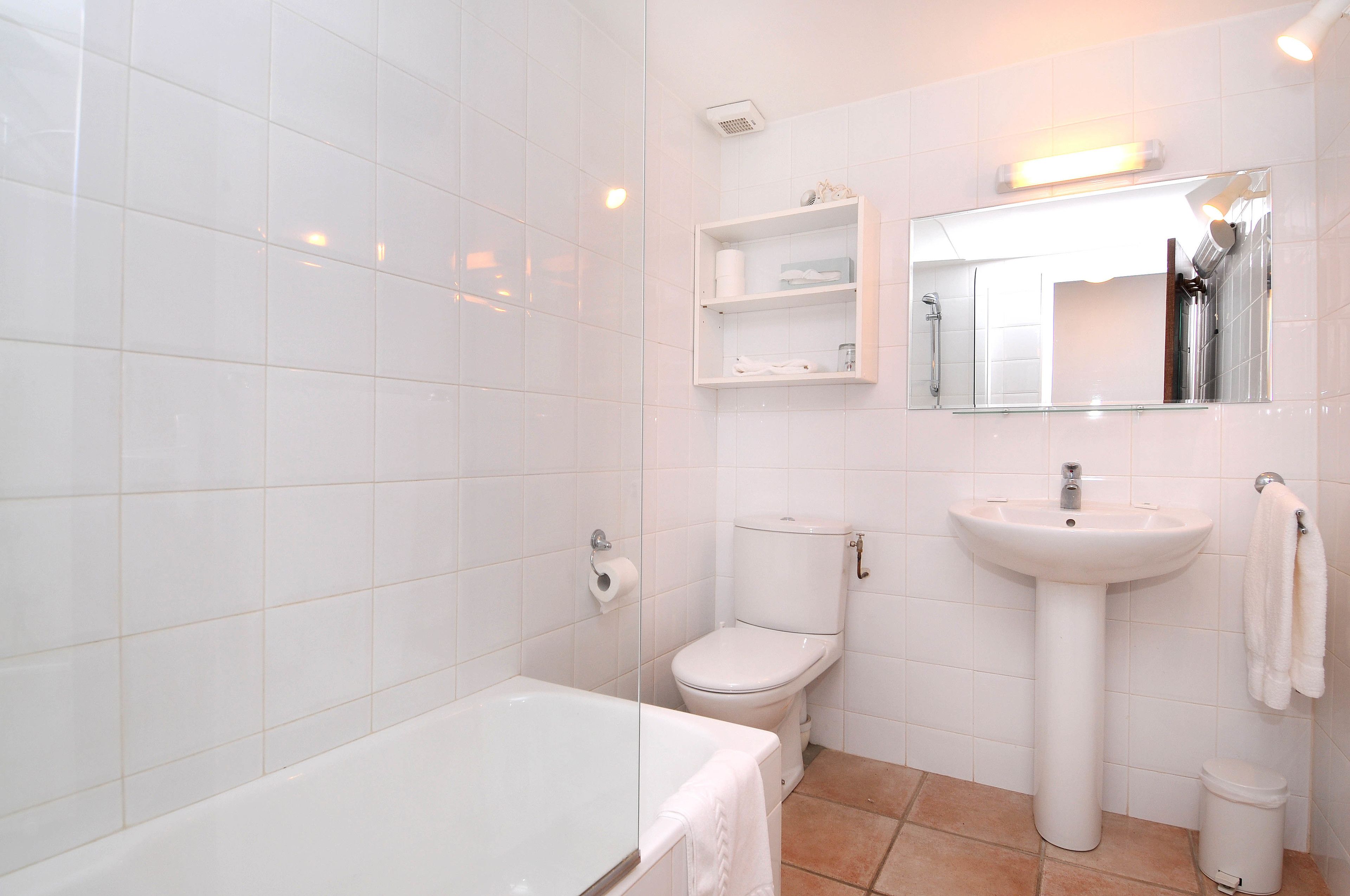 Un baño con azulejos blancos, una bañera, un inodoro, un lavabo y un espejo.