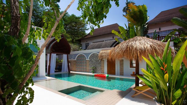 A swimming pool with a thatched roof structure, a white building with a tiled facade, and lush greenery. - Nagawari Art Maldives BBQ Pattaya Villa (Sattahip)