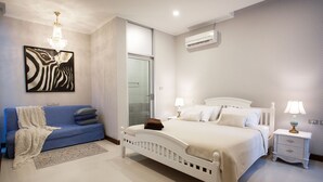 A bedroom with a bed, bedside tables, a nightstand, a sofa, a wall-mounted air conditioner, and a chandelier. - Nagawari Art Maldives BBQ Pattaya Villa (Sattahip)