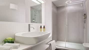 A modern bathroom with a large white sink, a glass shower enclosure, and a mirror above the sink.