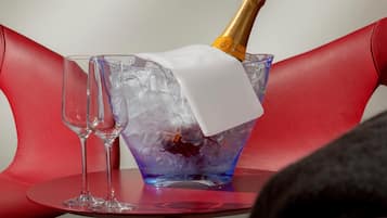 A bottle of champagne in a blue ice bucket on a red chair.